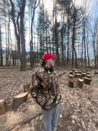 a man in a red cap is standing in a wooded area