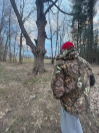 a man in a camouflage jacket walking through the woods